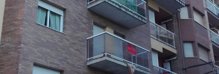 Bloc de pisos amb pancarta i rètols de "Es ven"